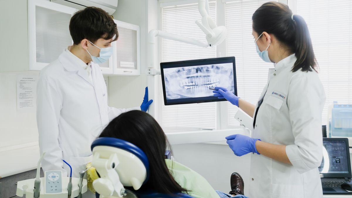 Two dentists reviewing a panoramic X-ray on a screen beside the patient chair